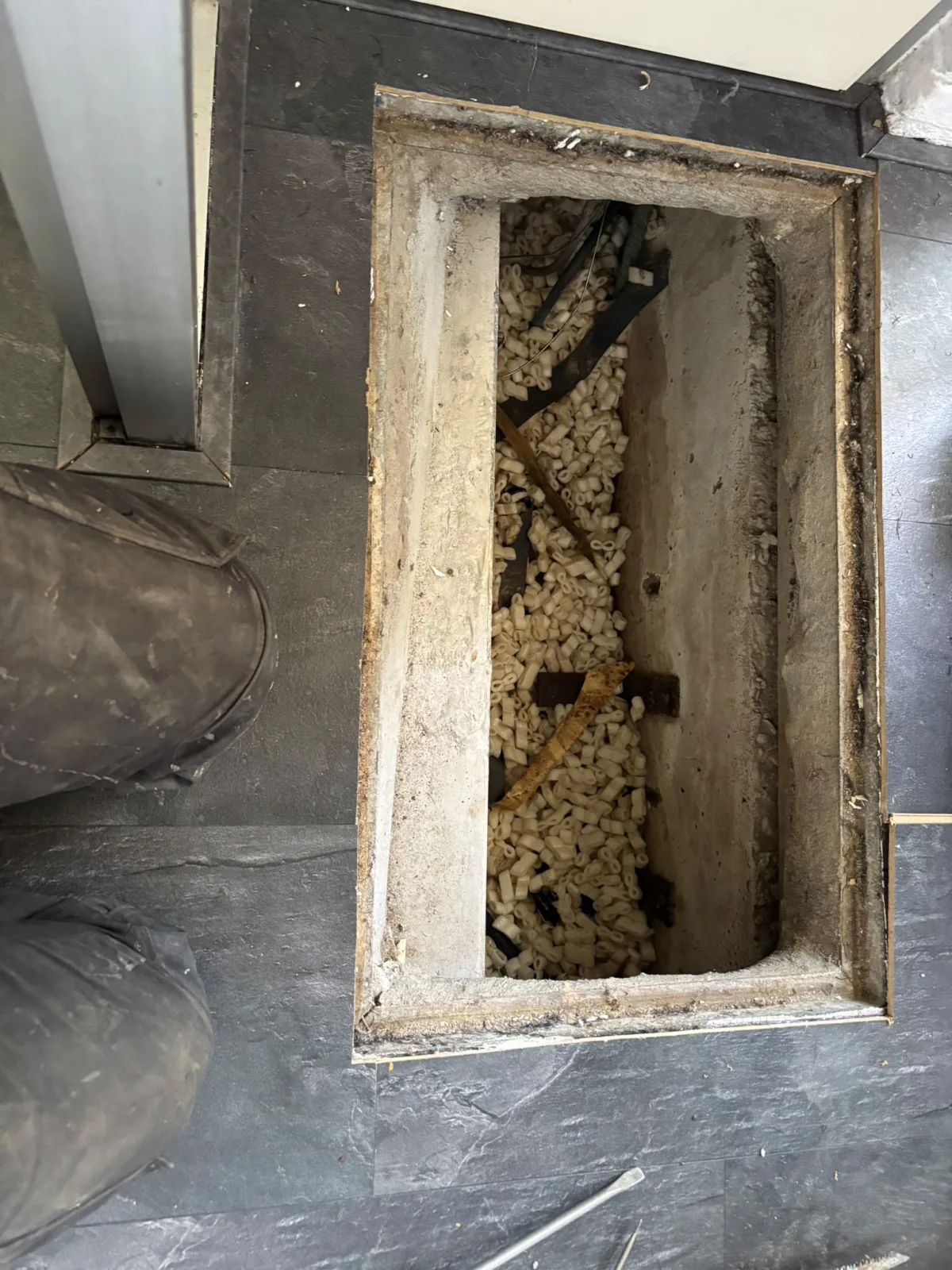 Open vloerluik toont kruipruimte of inspectieput gevuld met isolatiemateriaal en leidingen.